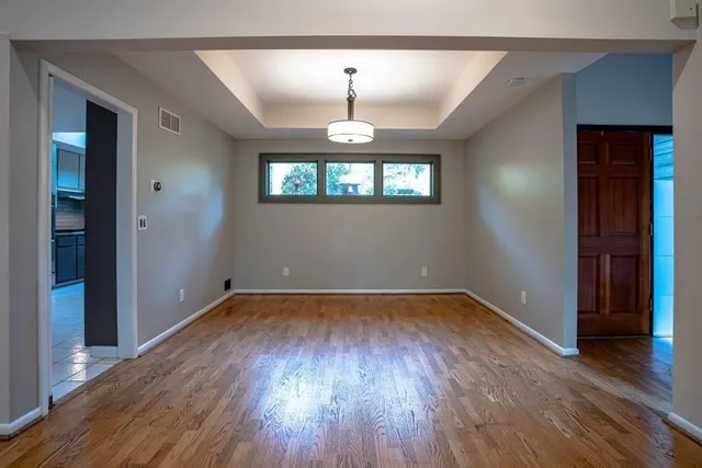 an empty room with wooden floor chandelier and windows