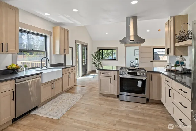 a large kitchen with stainless steel appliances granite countertop a stove a sink dishwasher a refrigerator and a dining table with wooden floor