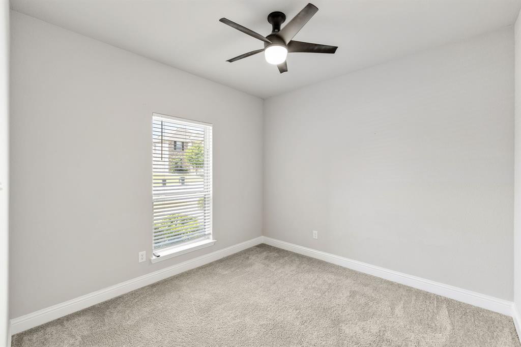 915 Timber Ridge Drive Justin, TX 76247 - Photo 30 of 39 Neutral-toned room featuring a single window with blinds, light-colored carpeting, a dark-toned ceiling fan with integrated lighting, and white baseboards