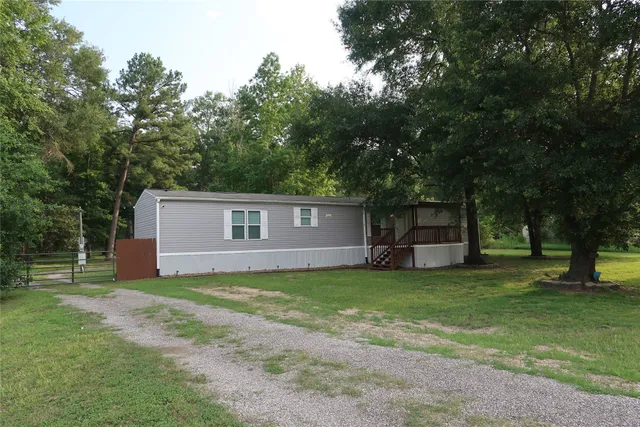 a house that is sitting in the grass with large trees and plants