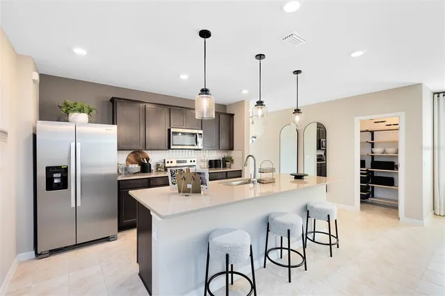 a kitchen with stainless steel appliances a refrigerator a sink a stove and chairs with wooden floor