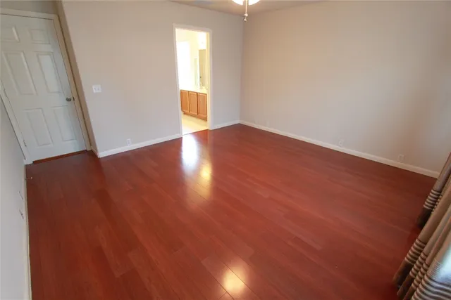 an empty room with wooden floor and windows with curtains