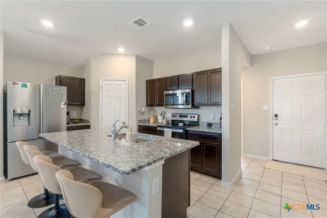 a kitchen with granite countertop kitchen island stainless steel appliances a stove refrigerator sink and cabinets