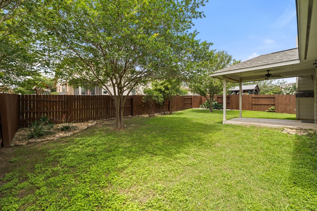 347 Spring Drive Kyle, TX 78640 - Photo 37 of 40 A spacious backyard features mature trees and a covered patio, ideal for outdoor relaxation.