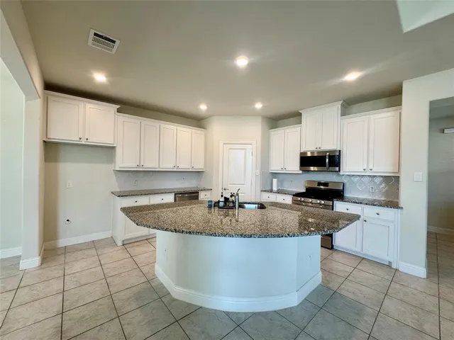 a kitchen with kitchen island granite countertop a stove a sink a counter top space and cabinets