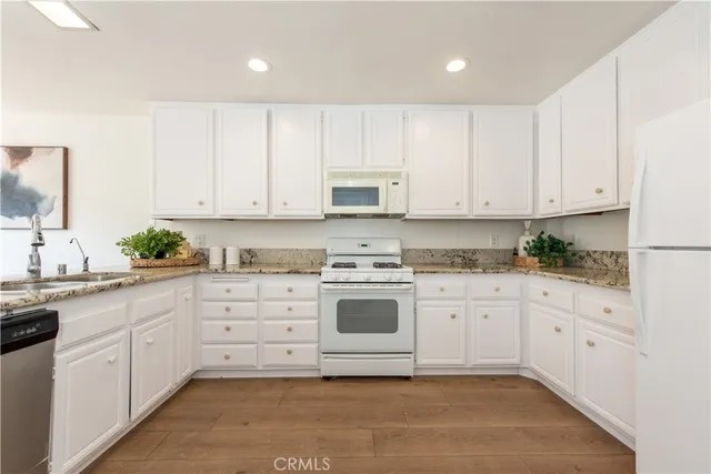 a white kitchen with granite top and stainless steel appliances