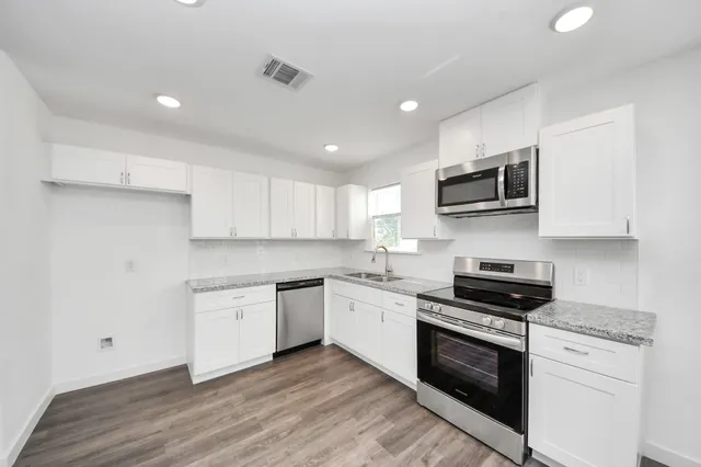 a kitchen with granite countertop a sink wooden floor and stainless steel appliances