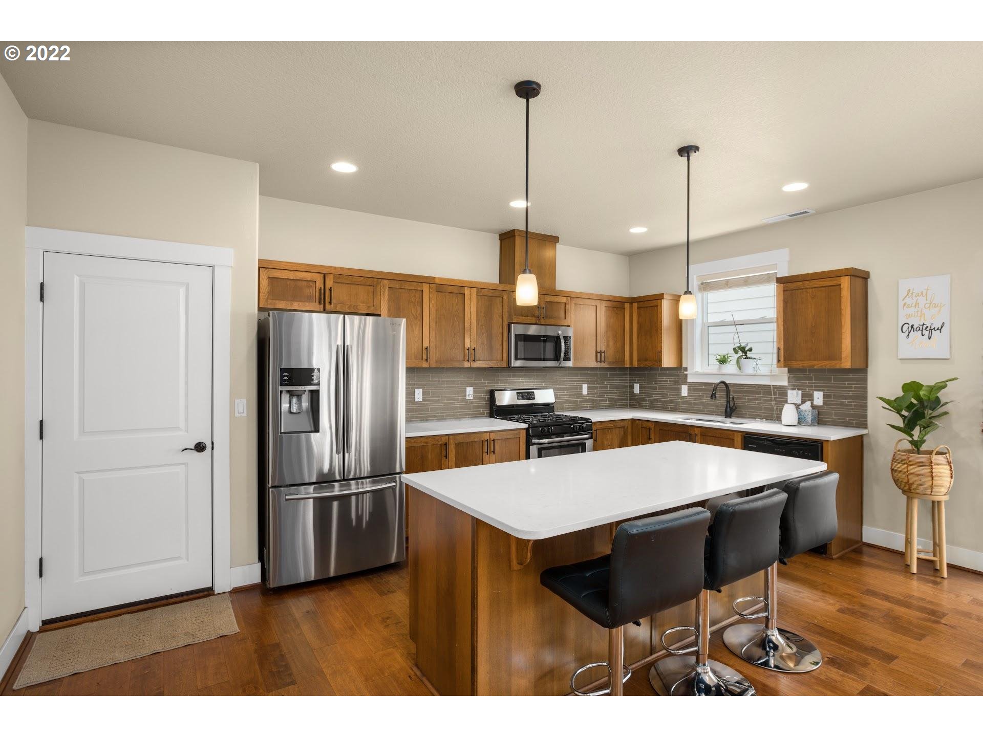 374 Southwest 202nd Terrace Beaverton, OR 97006 - Photo 9 of 28 a kitchen with stainless steel appliances kitchen island granite countertop a refrigerator a stove a sink a dining table and chairs with wooden floor