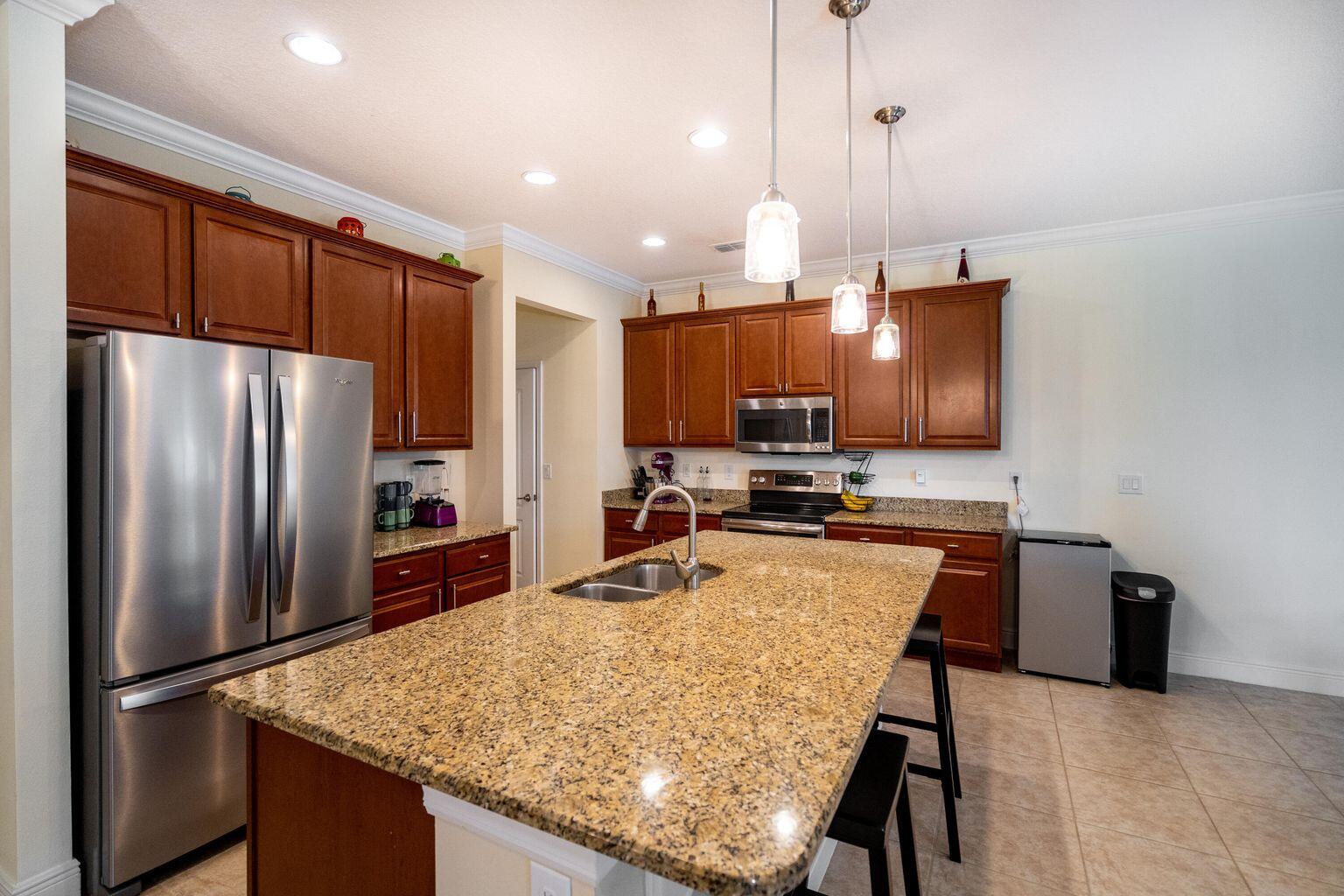 1026 Southwest Ingrassina Avenue Port St. Lucie, FL 34953 - Photo 5 of 20 a kitchen with stainless steel appliances granite countertop a refrigerator oven a sink dishwasher a dining table and chairs with wooden floor