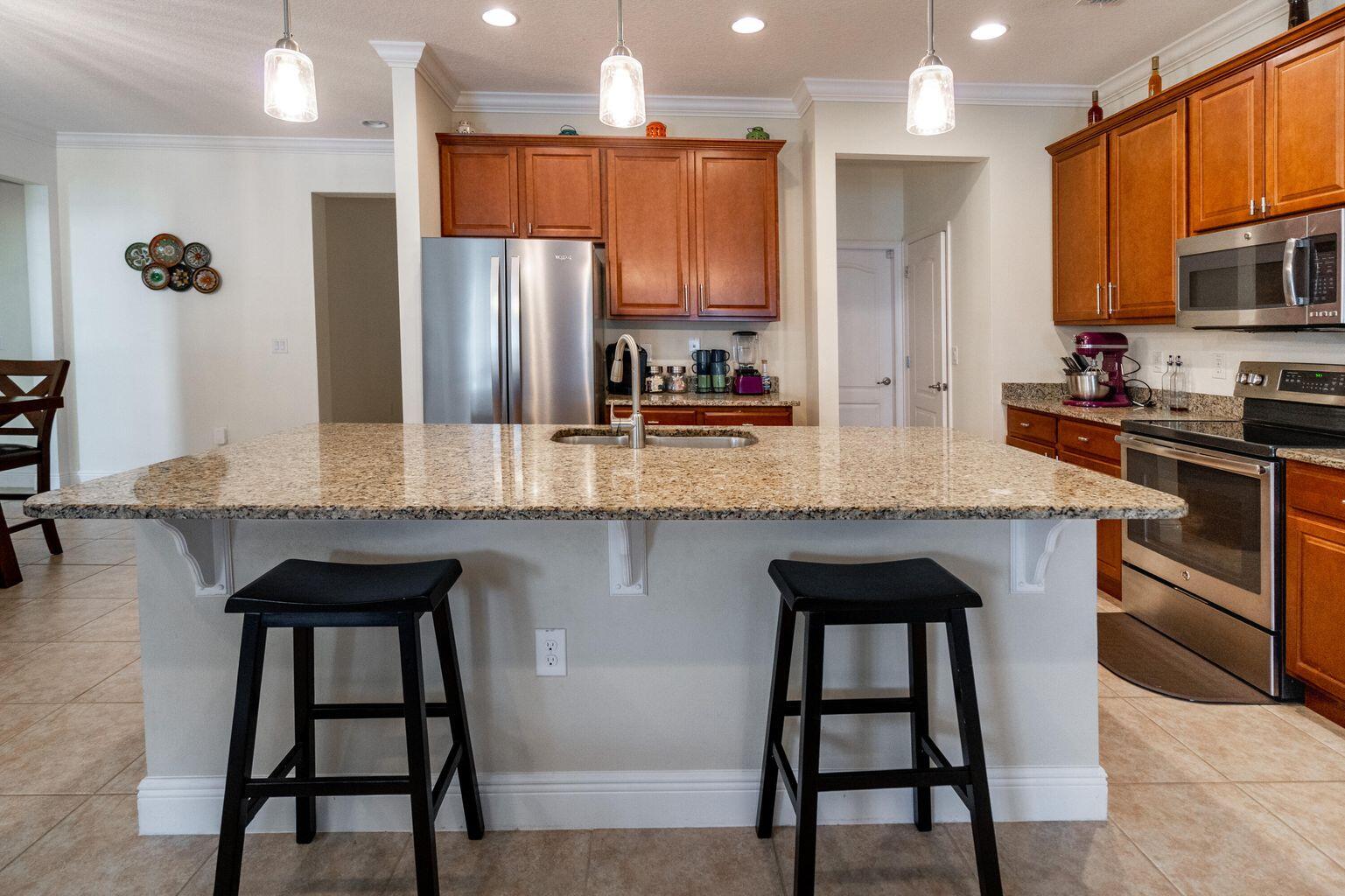 1026 Southwest Ingrassina Avenue Port St. Lucie, FL 34953 - Photo 6 of 20 a kitchen with stainless steel appliances granite countertop a stove top oven a refrigerator a sink and chairs