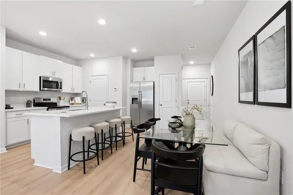 a kitchen with stainless steel appliances kitchen island granite countertop a stove a sink a refrigerator and white cabinets with wooden floor