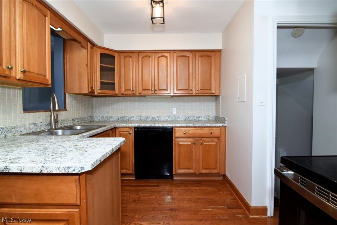 5284 Edenhurst Road Lyndhurst, OH 44124 - Photo 13 of 50 Kitchen featuring wood cabinetry, light-toned stone countertops, a stainless steel sink with a gooseneck faucet, a black dishwasher, and wood-finish flooring