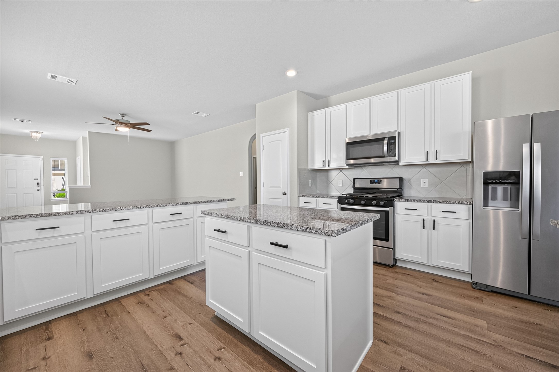 2526 Sturgeon Way Conroe, TX 77384 - Photo 3 of 49 This modern kitchen features sleek white cabinetry, granite countertops, and stainless steel appliances. The open layout with a central island and wood flooring offers a spacious and inviting atmosphere.