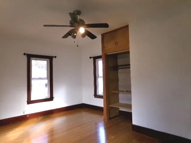 an empty room with wooden floor chandelier fan and windows
