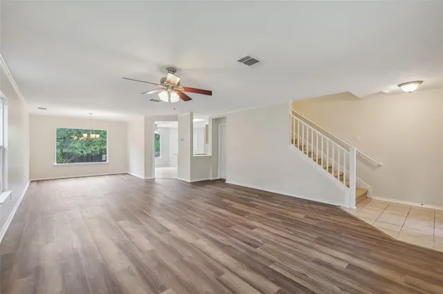 a view of an empty room with wooden floor and a chandelier fan