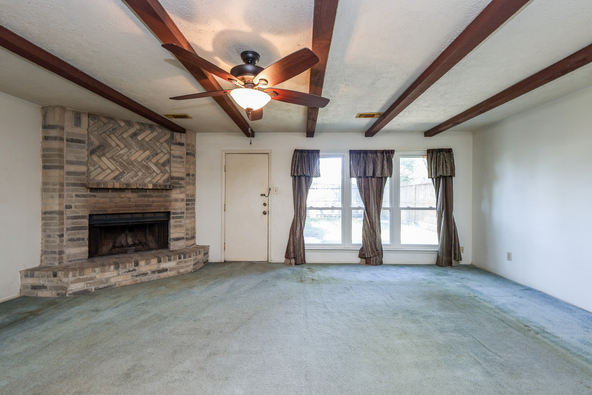 21422 Bridgepoint Lane Spring, TX 77388 - Photo 8 of 20 Spacious living room with a cozy brick fireplace, exposed wood beams, and large windows offering plenty of natural light.