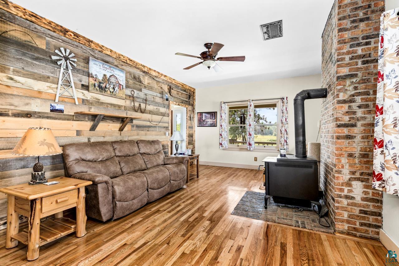 33415 Jackson Road Askov, MN 55704 - Photo 34 of 91 Living area featuring a wood stove, ceiling fan, wood finished floors, and wood walls