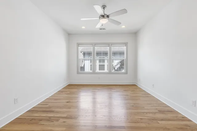an empty room with wooden floor chandelier fan and windows