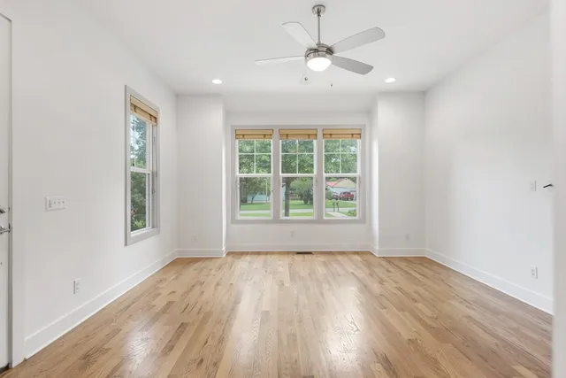 an empty room with wooden floor chandelier fan and windows