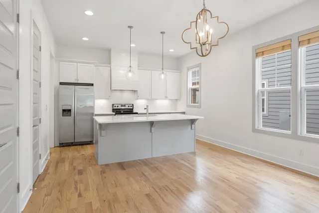 a kitchen with stainless steel appliances granite countertop a refrigerator a sink dishwasher a stove and white cabinets with wooden floor