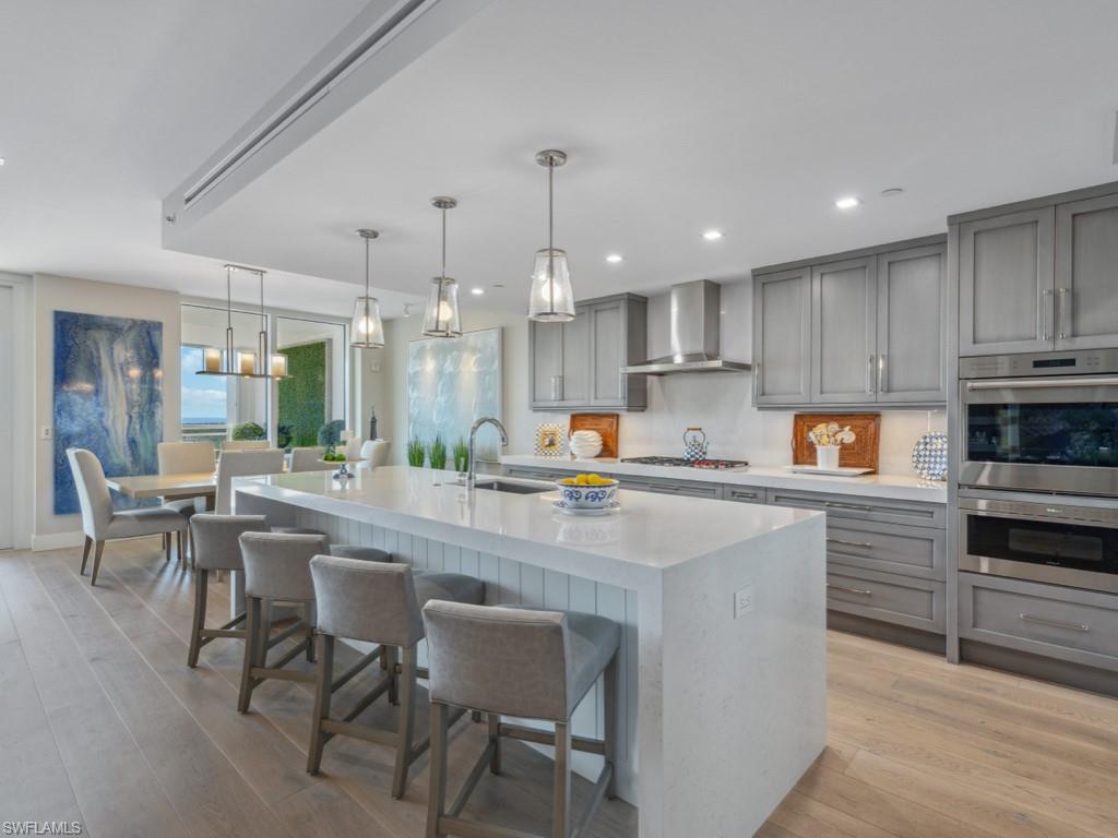 13915 Old Coast Road, Unit 702 Naples, FL 34110 - Photo 9 of 20 Kitchen with gray cabinetry, light wood-type flooring, a kitchen breakfast bar, light stone countertops, and recessed lighting