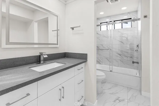 a bathroom with a granite countertop sink a toilet a mirror and shower