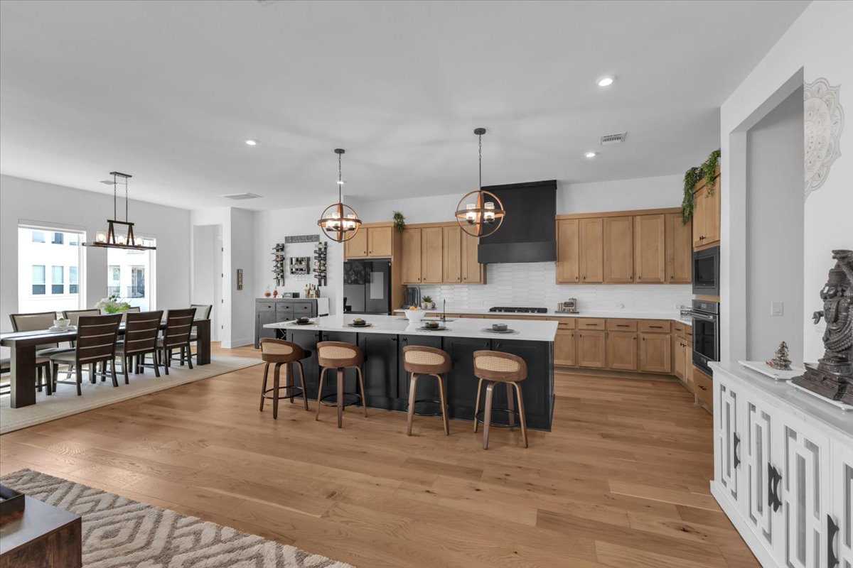 2312 Mondello Path Leander, TX 78641 - Photo 22 of 40 Two tone kitchen featuring suspended lighting, two tone cabinets, a breakfast bar, an island with sink, and light wood-style floors