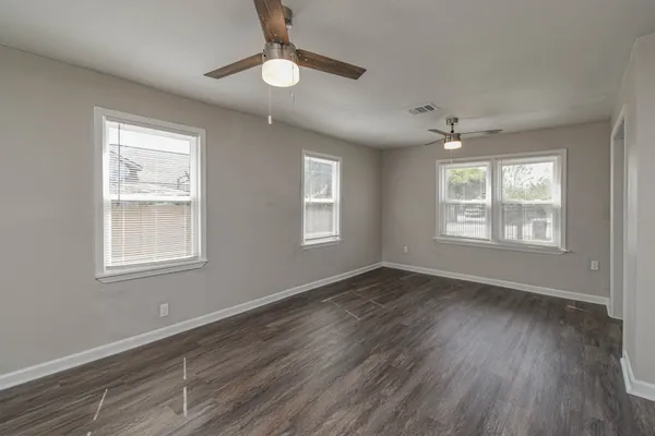 an empty room with wooden floor chandelier fan and windows