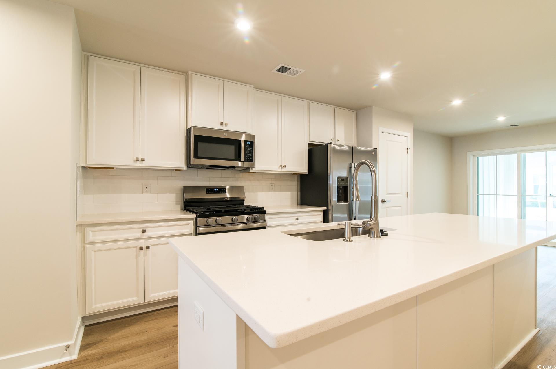 2382 Elowen Lane Longs, SC 29568 - Photo 4 of 36 Kitchen featuring stainless steel appliances, white cabinetry, light wood finished floors, an island with sink, and tasteful backsplash