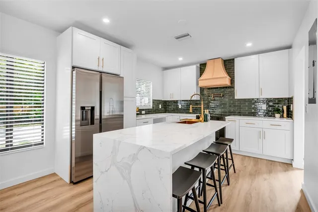 a kitchen with stainless steel appliances a refrigerator a stove a sink a dining table and chairs with wooden floor