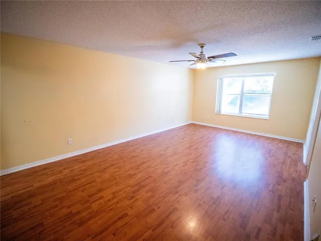 an empty room with wooden floor ceiling fan and windows