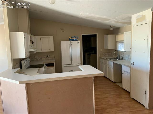 17610 Hanover Road Colorado Springs, CO 80928 - Photo 15 of 16 Kitchen featuring white cabinetry, sink, white appliances, light hardwood / wood-style floors, and exhaust hood