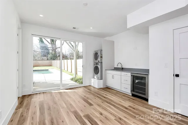 a view of an empty room and a kitchen with wooden floor and a window