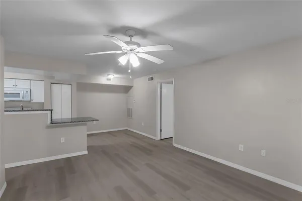an empty room with wooden floor a ceiling fan and kitchen view
