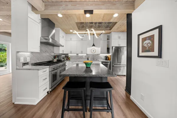 a kitchen with stainless steel appliances a stove a refrigerator and a dining table with wooden floor