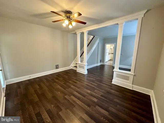 a view of an empty room with wooden floor and a ceiling fan