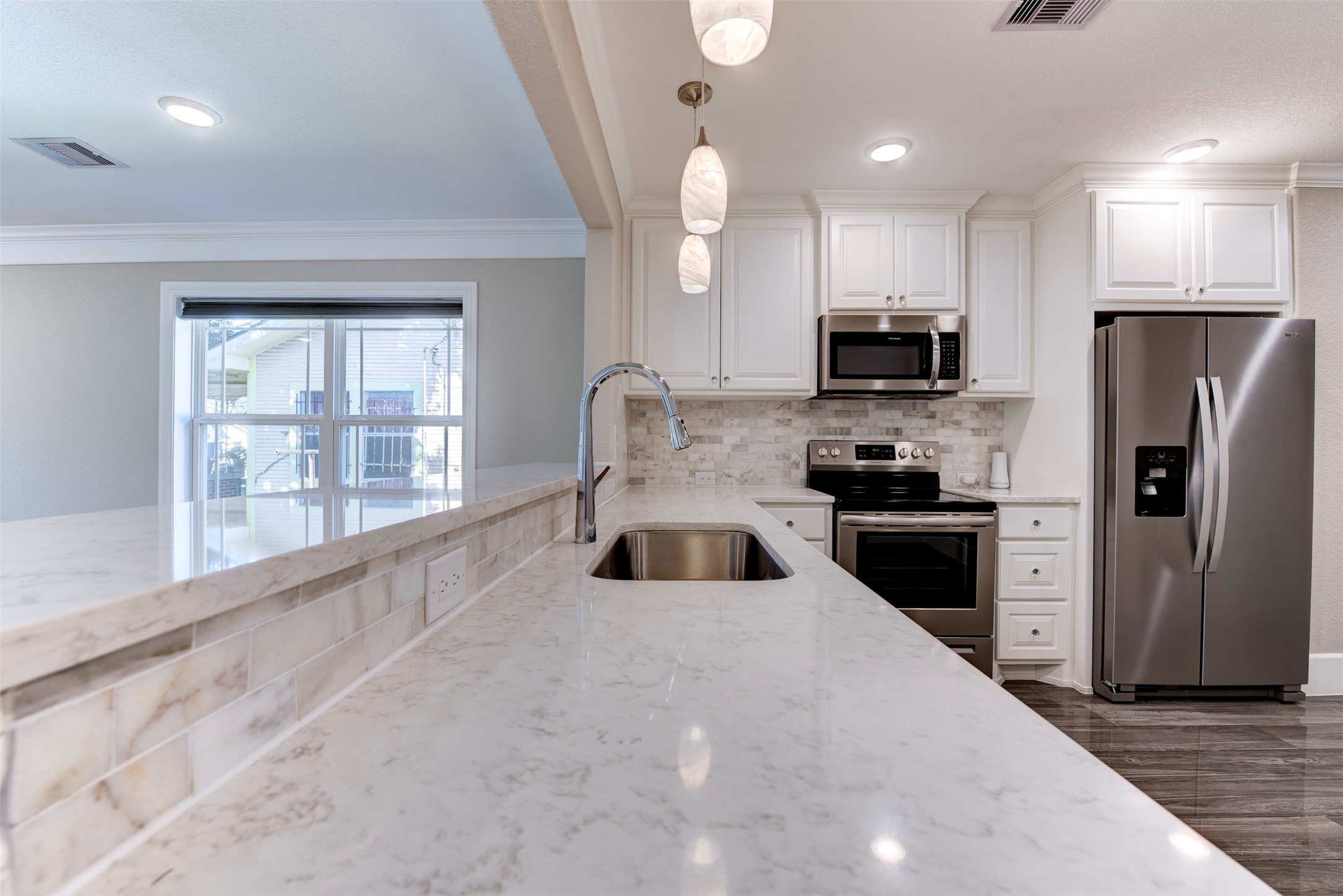 109 Dresden Street Houston, TX 77012 - Photo 19 of 43 This modern kitchen features sleek stainless steel appliances, white cabinetry, and a spacious marble countertop with a built-in sink. Pendant lighting adds elegance, while the open layout offers a bright and airy feel, perfect for entertaining.