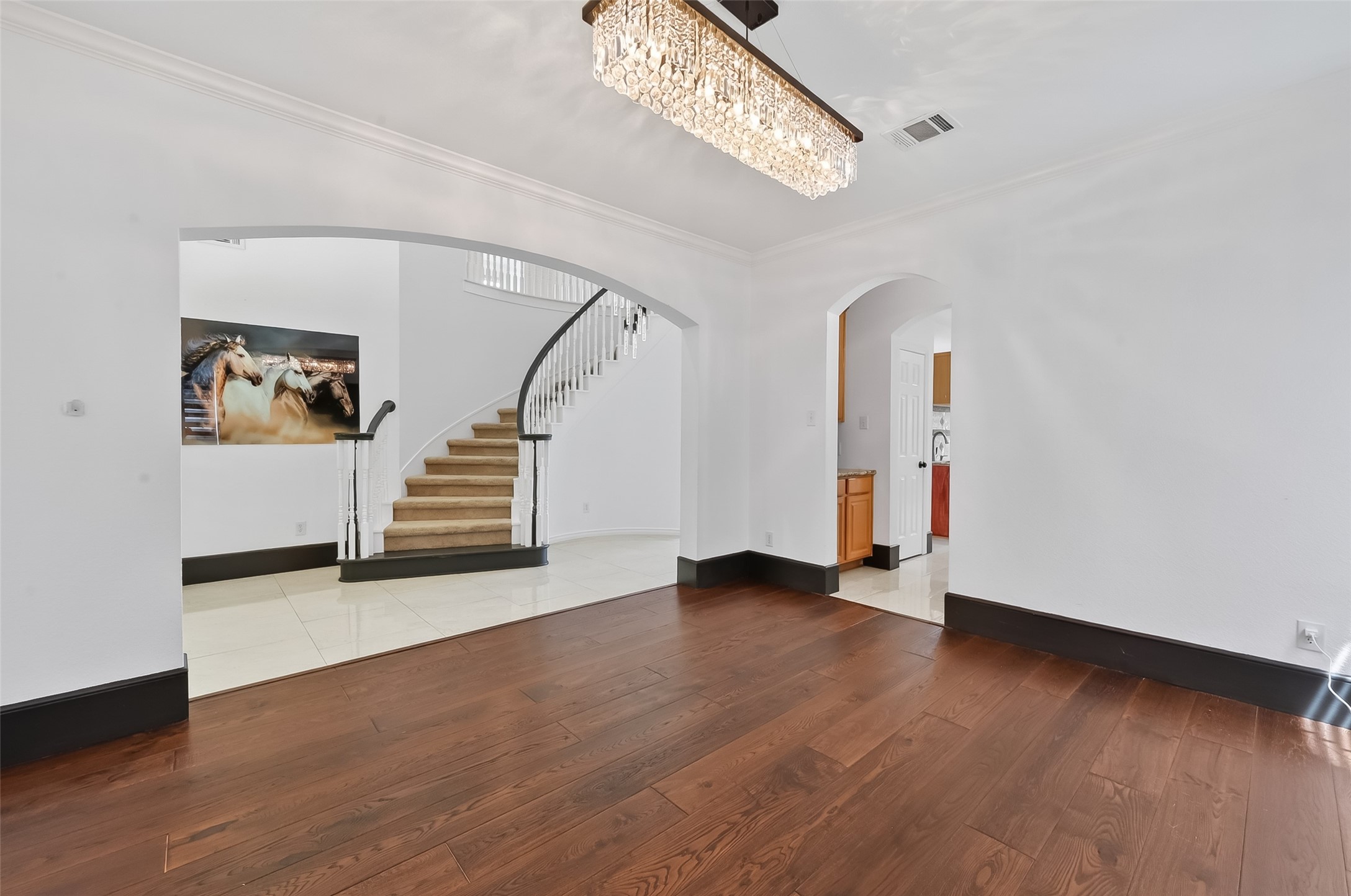 1311 Rene Court Sugar Land, TX 77479 - Photo 6 of 45 This photo showcases a spacious formal dining room with elegant hardwood floors and a striking chandelier. It features arched doorways leading to different areas, including a view of a curved staircase with a modern railing, adding a touch of sophistication.