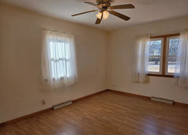 an empty room with wooden floor fan and windows