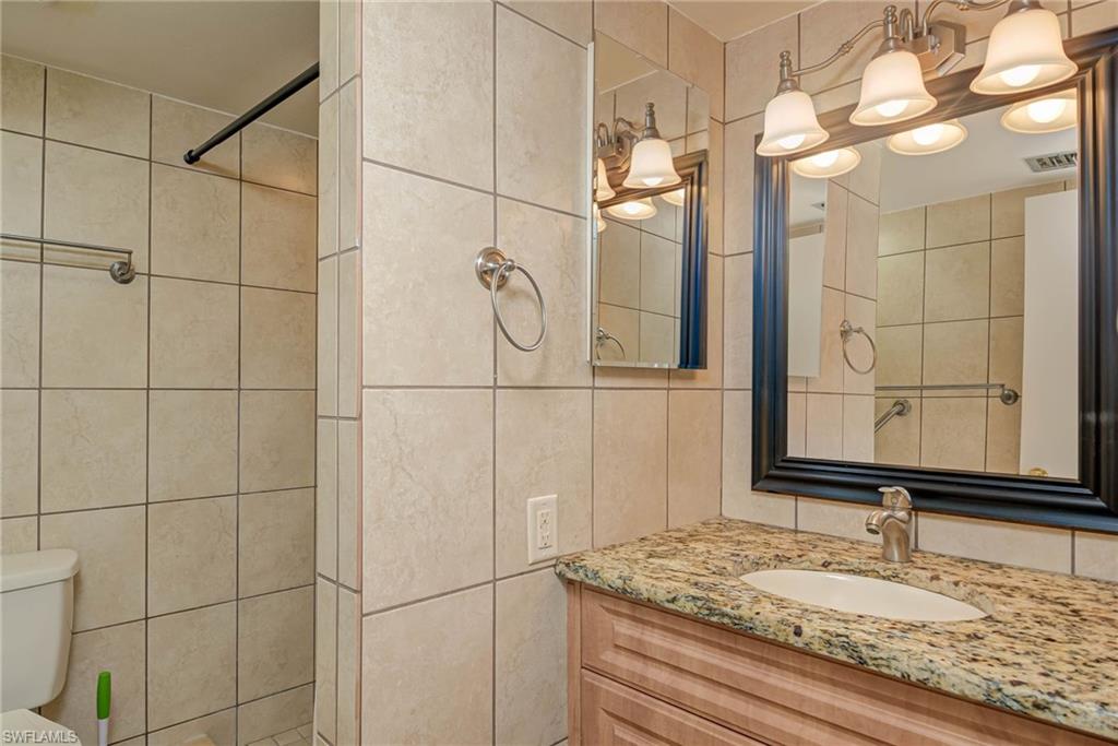 3030 Binnacle Drive, Unit 305 Naples, FL 34103 - Photo 20 of 25 a bathroom with a granite countertop sink a mirror and shower