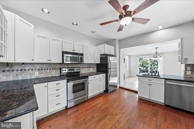 a kitchen with stainless steel appliances white cabinets a sink a stove a refrigerator and microwave with wooden floor