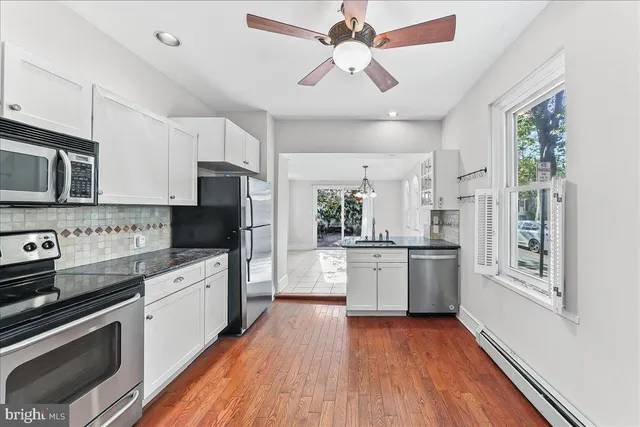 a kitchen with stainless steel appliances granite countertop a refrigerator a stove top oven a sink dishwasher and white cabinets with wooden floor
