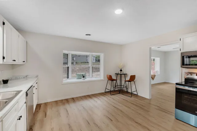 a view of a kitchen and an empty room with wooden floor and a window