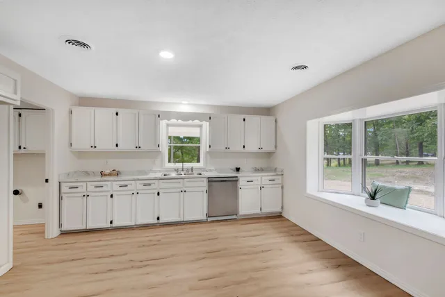 a large kitchen with granite countertop a stove a sink and white cabinets with wooden floor