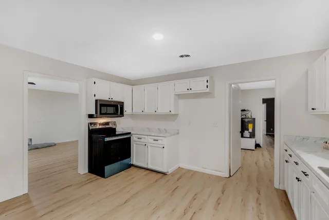 a kitchen with stainless steel appliances a stove top oven a sink a refrigerator white cabinets and wooden floor