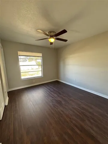 an empty room with wooden floor chandelier fan and windows