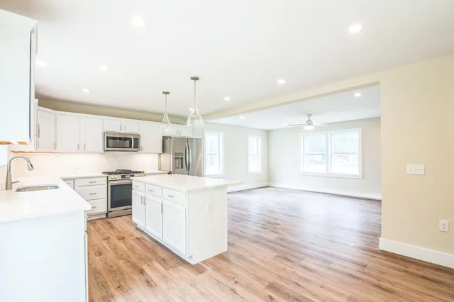 a large kitchen with stainless steel appliances granite countertop a stove a sink dishwasher and a oven with white cabinets