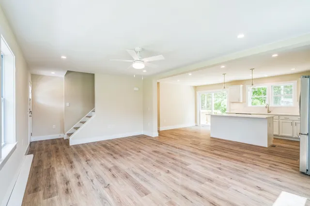 a view of an empty room with wooden floor and a kitchen