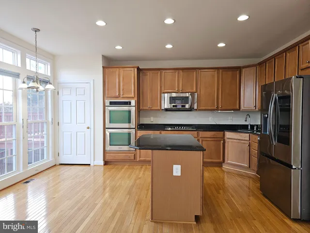 a kitchen with stainless steel appliances granite countertop a refrigerator microwave and wooden floor