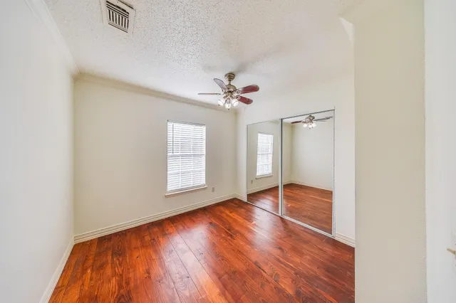 an empty room with wooden floor fan and windows